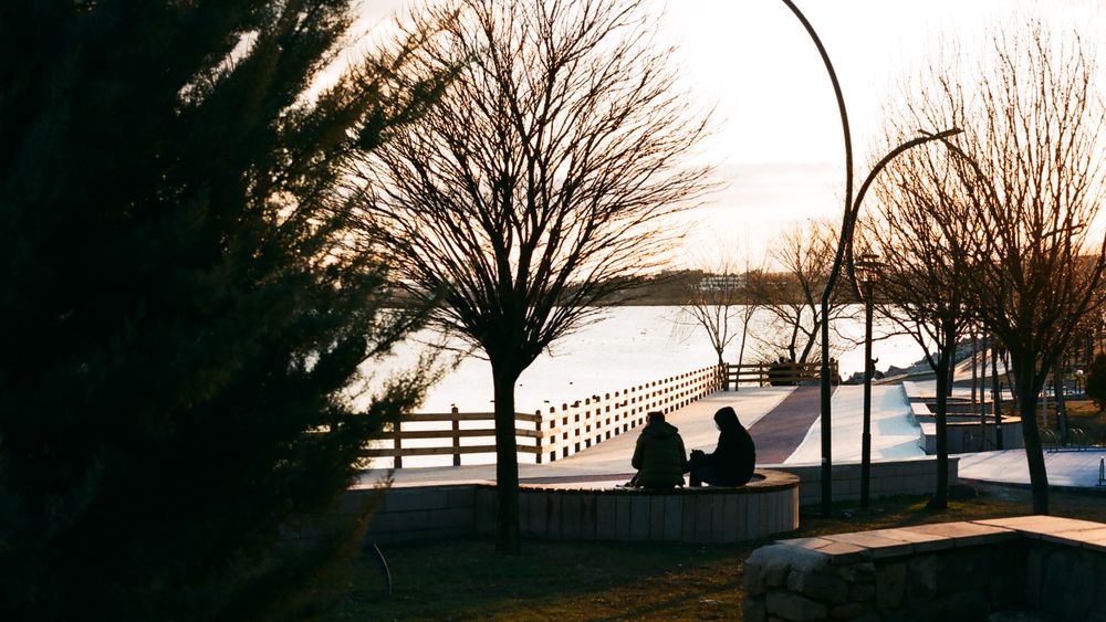 Dos siluetas sentadas juntas frente a un lago al anochecer