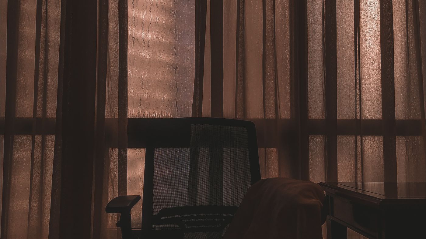 La silueta de una silla vacia frente a una ventana en una habitacion a oscuras