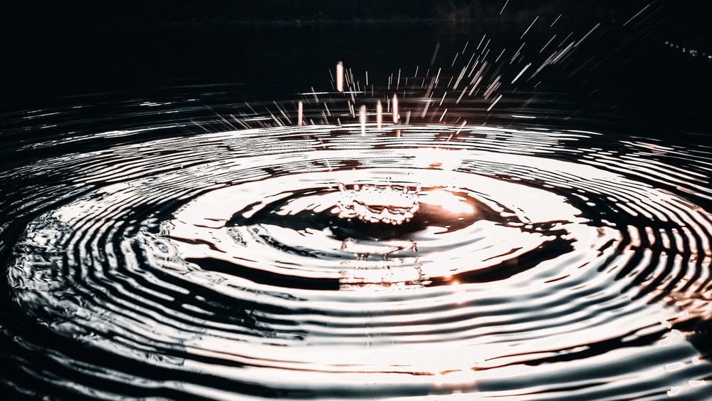 Una gota cayendo sobre agua oscura y las ondas que abre