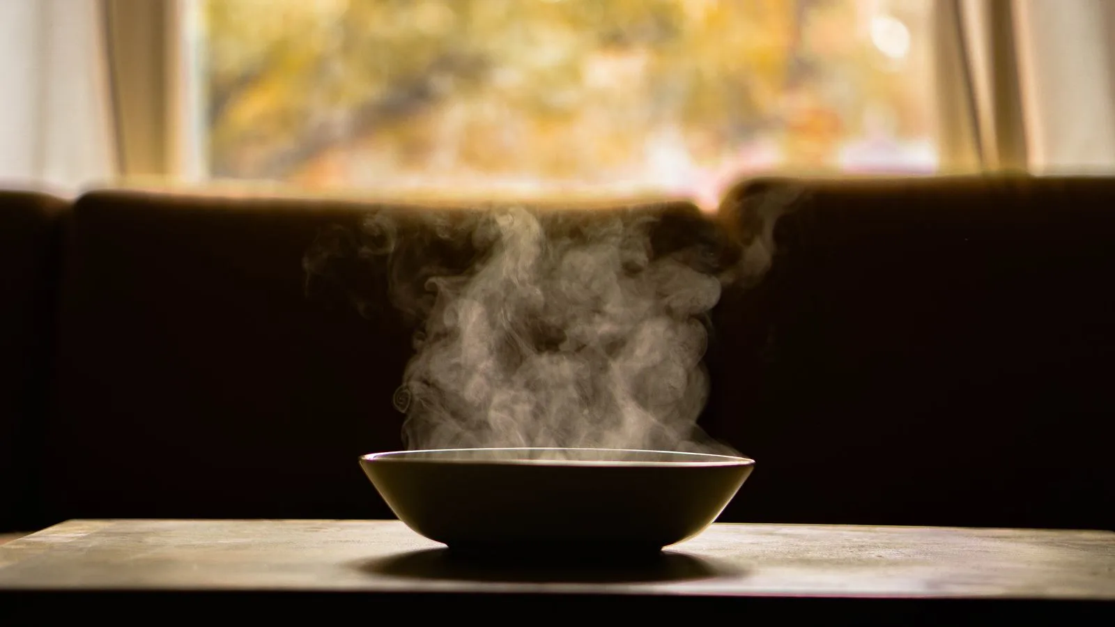 Un cuenco humeante sobre una mesa oscura, con el vapor subiendo a contraluz
