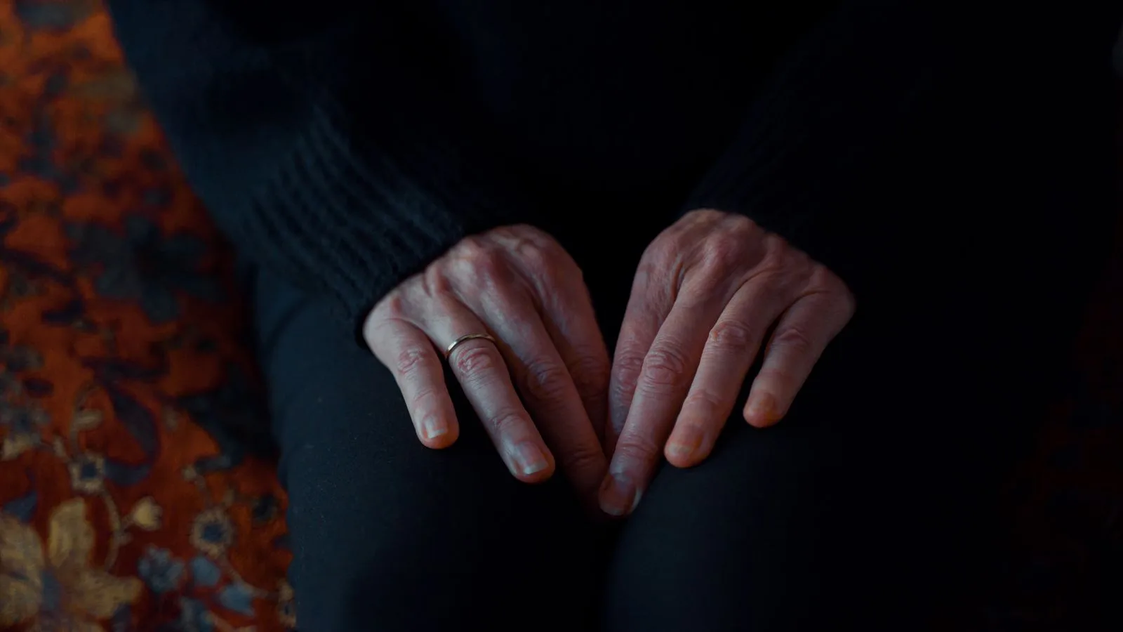 Unas manos en reposo sobre el regazo, sobre fondo oscuro