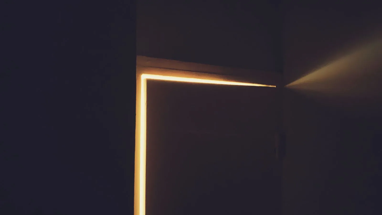 Luz cálida saliendo por una puerta entreabierta en una habitación a oscuras