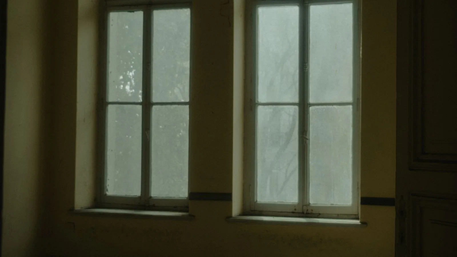 Dos ventanas de una habitación vacía en penumbra, con luz difusa entrando por los cristales