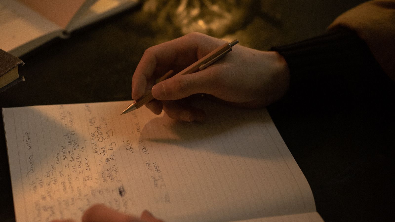 Unas manos escribiendo en un cuaderno a la luz de una vela