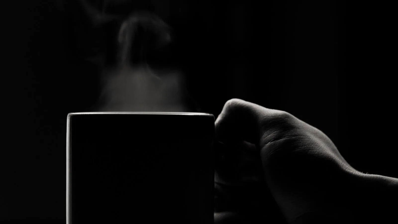 Una mano sosteniendo una taza a contraluz, en penumbra