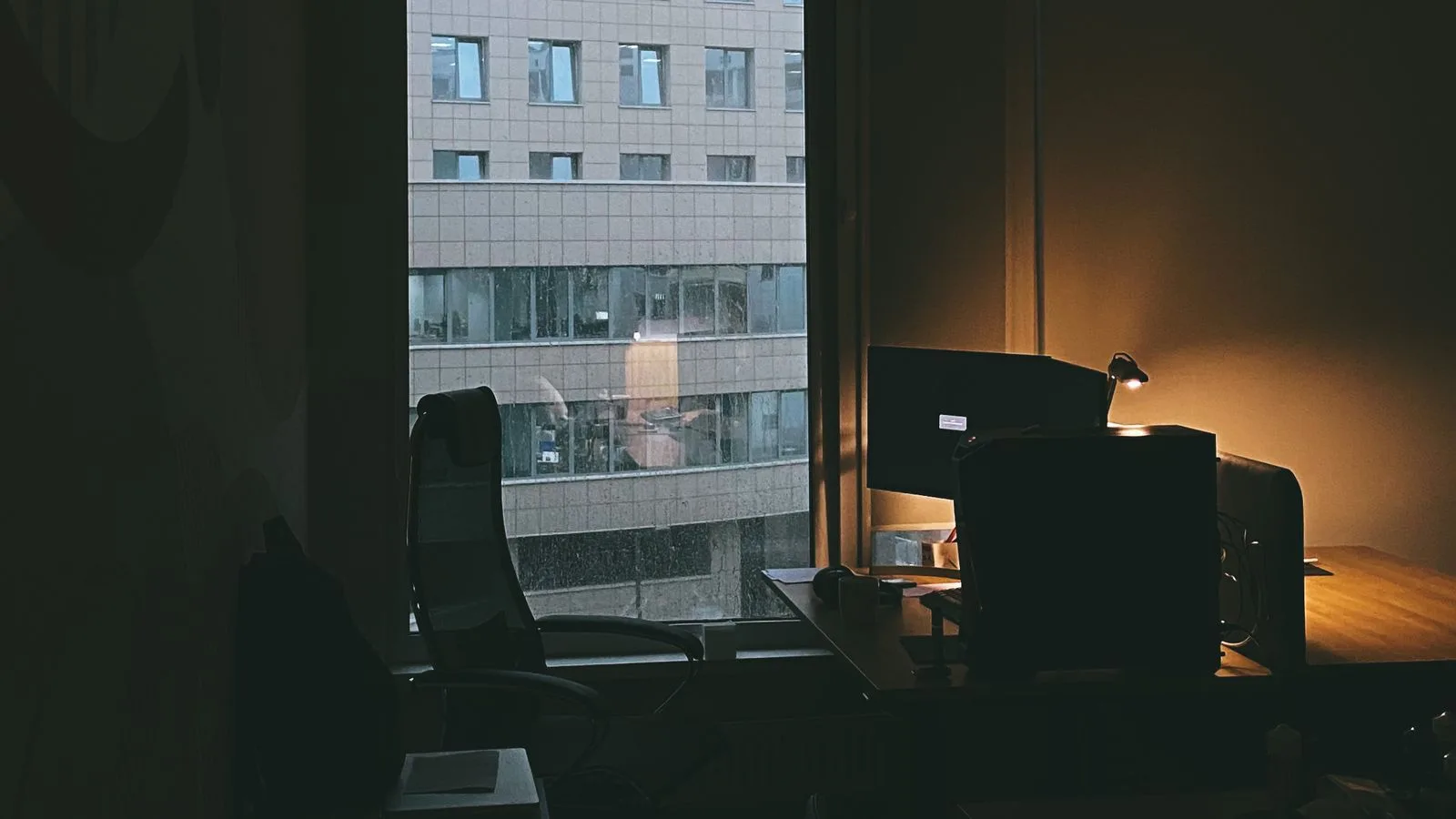 Un puesto de trabajo vacío en una oficina en penumbra, con el edificio de enfrente por la ventana