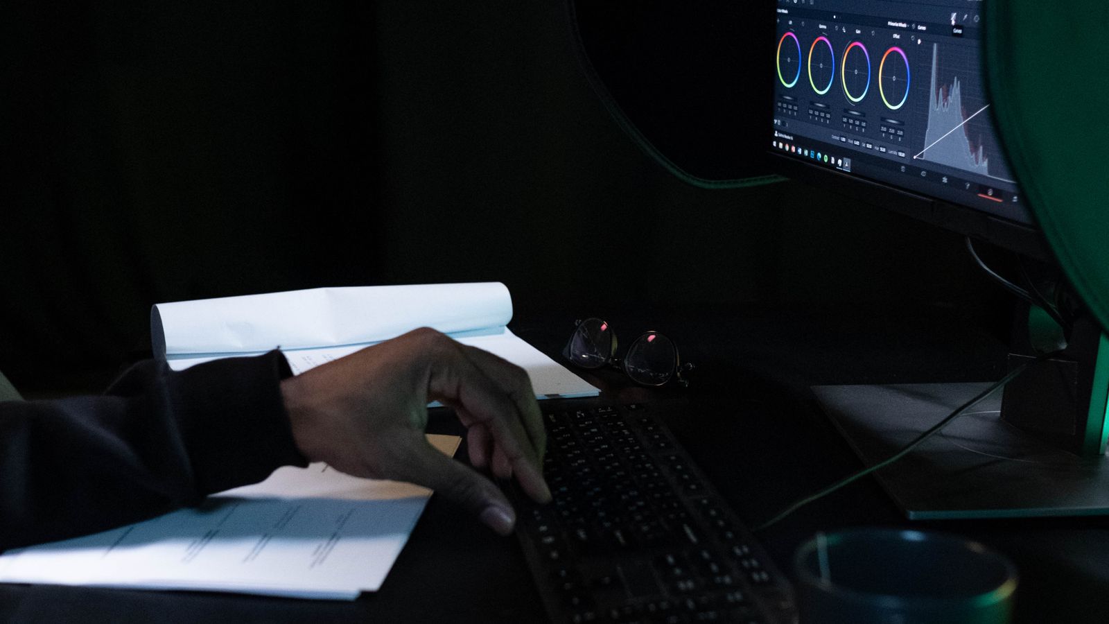 Una mano editando video ante un monitor en una habitacion a oscuras