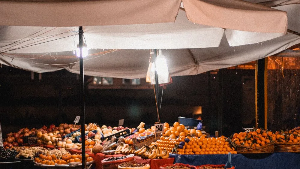 Un puesto de fruta de mercado por la noche, iluminado bajo el toldo