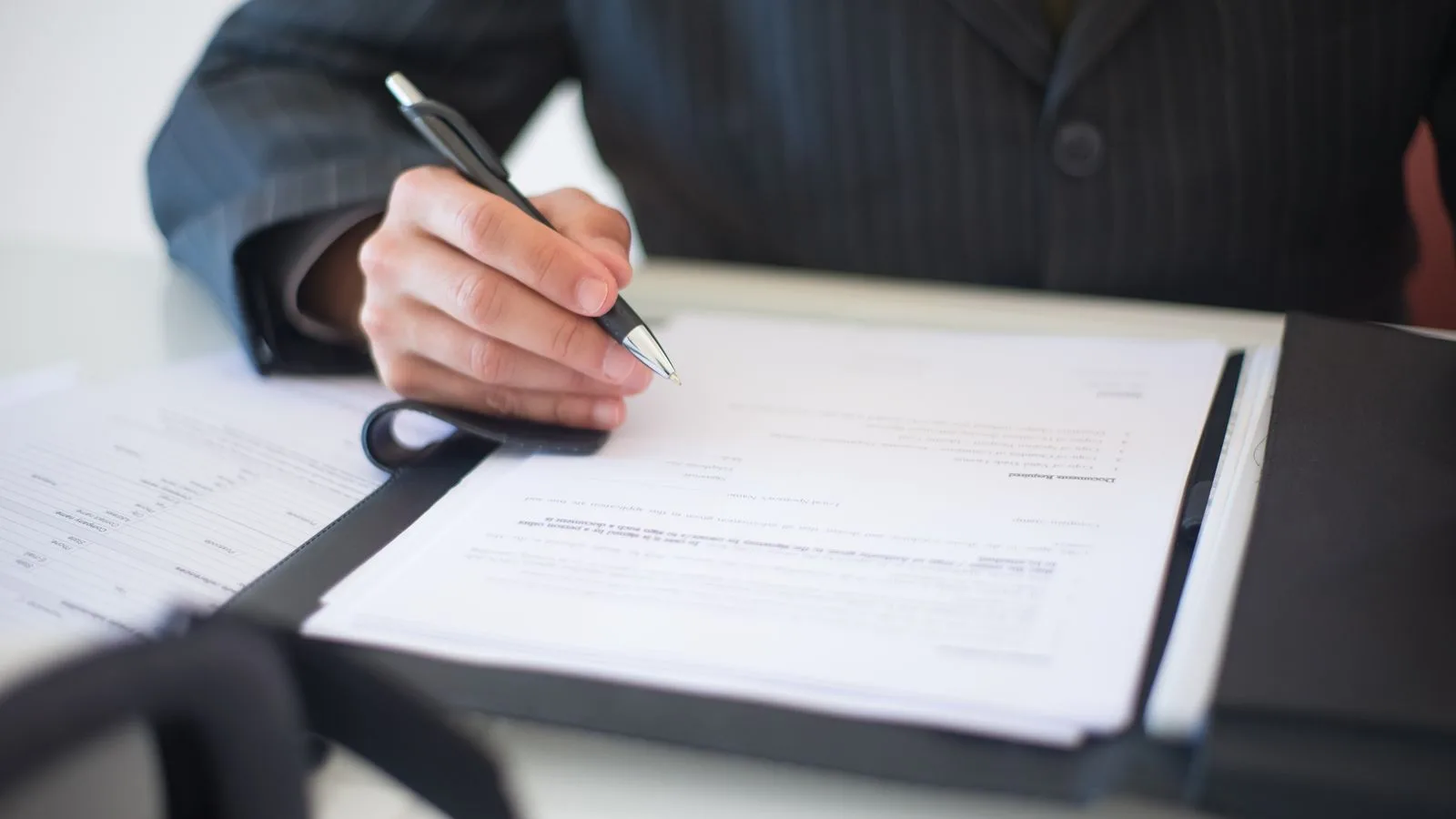 Una mano firmando un documento sobre un escritorio en penumbra