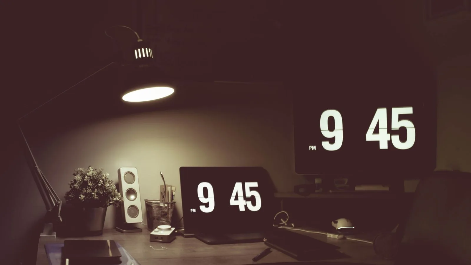 Un reloj de solapas marcando las 9:45 sobre un escritorio a oscuras, iluminado por una lampara