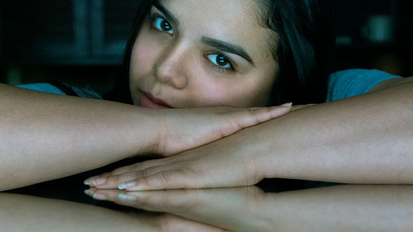 Una mujer joven apoyada en sus brazos, con la mirada baja, en luz tenue