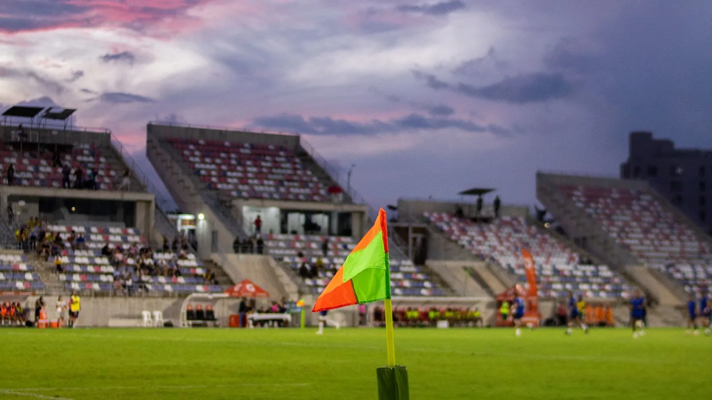 Un estadio de fútbol al atardecer, con el banderín de córner en primer plano