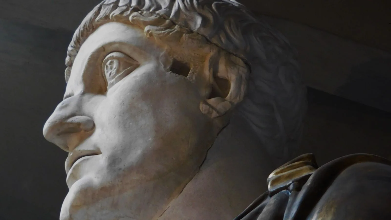 Un busto de mármol romano de perfil, iluminado sobre fondo oscuro