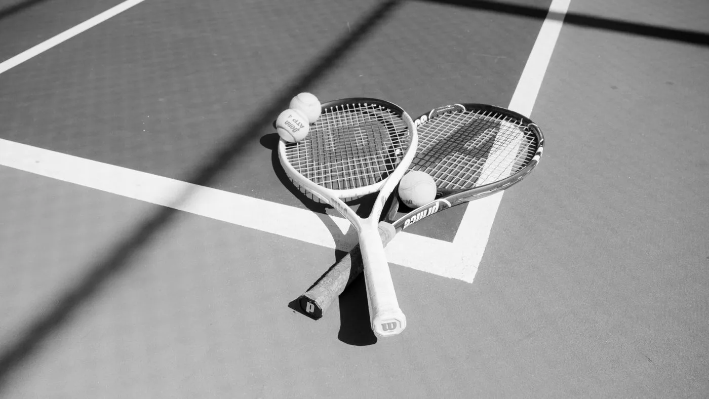 Dos raquetas y varias pelotas de tenis sobre la cancha, en blanco y negro
