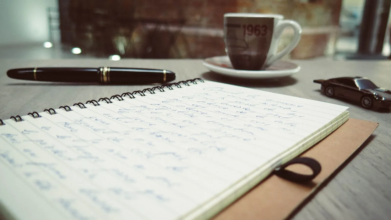 Un cuaderno con notas escritas a mano, una pluma y una taza de café sobre el escritorio