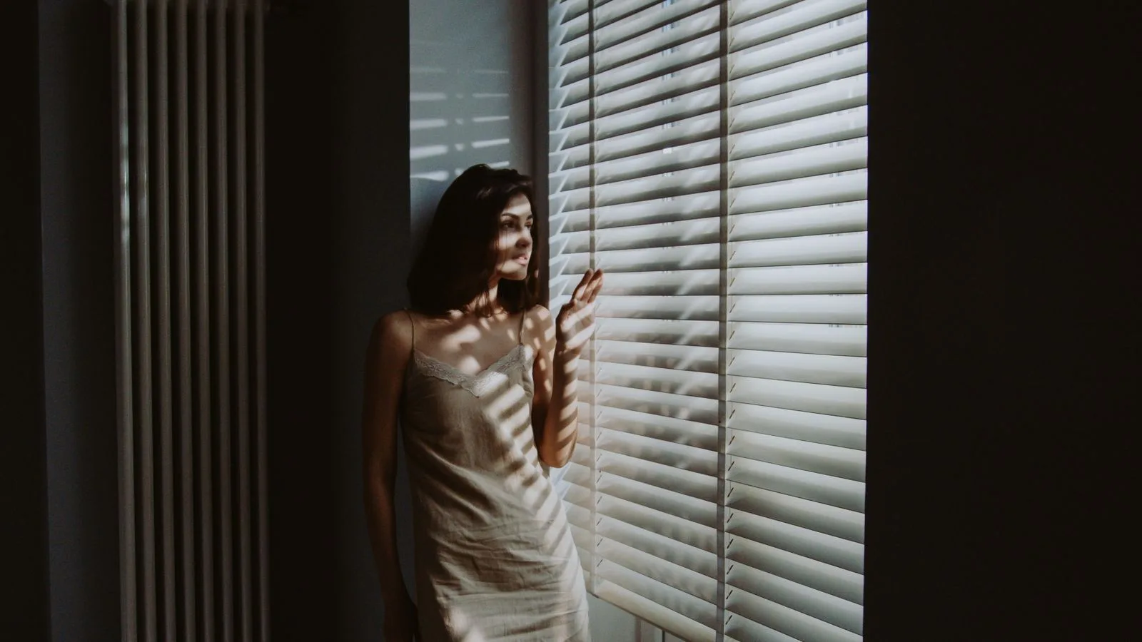 Una mujer de pie junto a una ventana, con luz cálida y suave