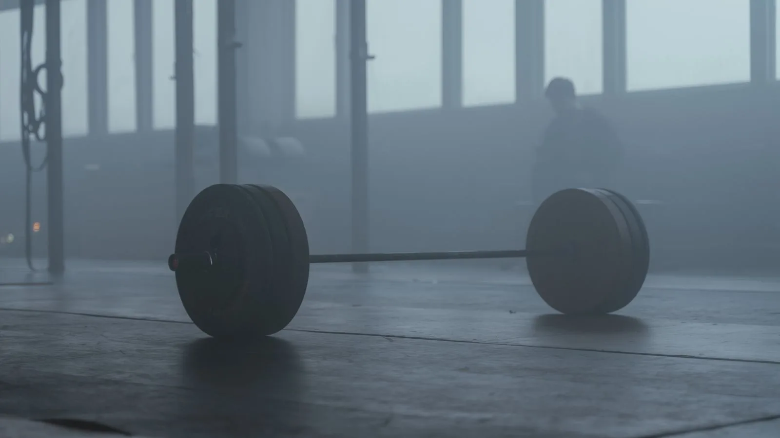 Una barra sola en el suelo de un gimnasio oscuro, entre neblina