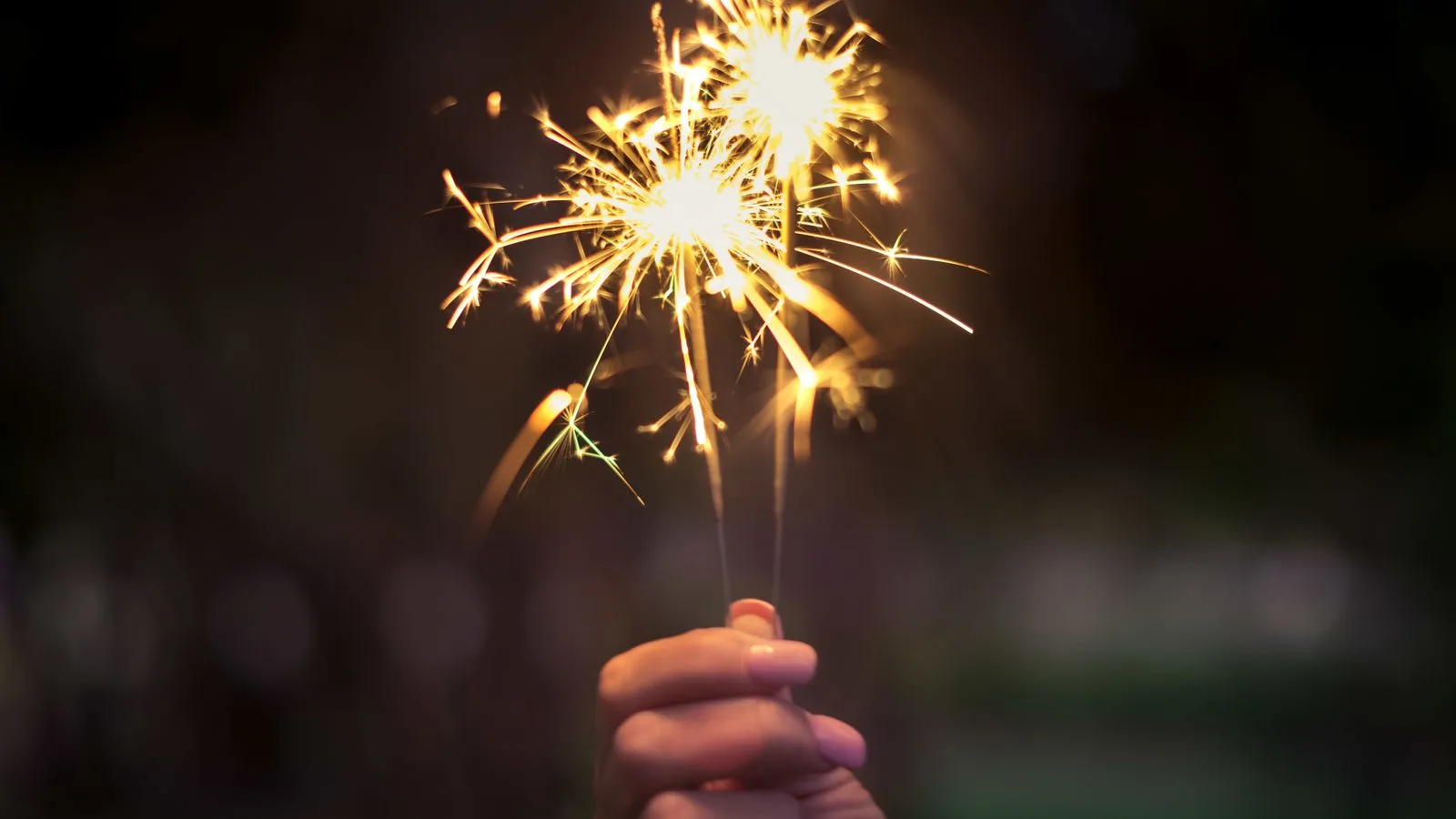 Una mano sostiene dos bengalas encendidas en la noche