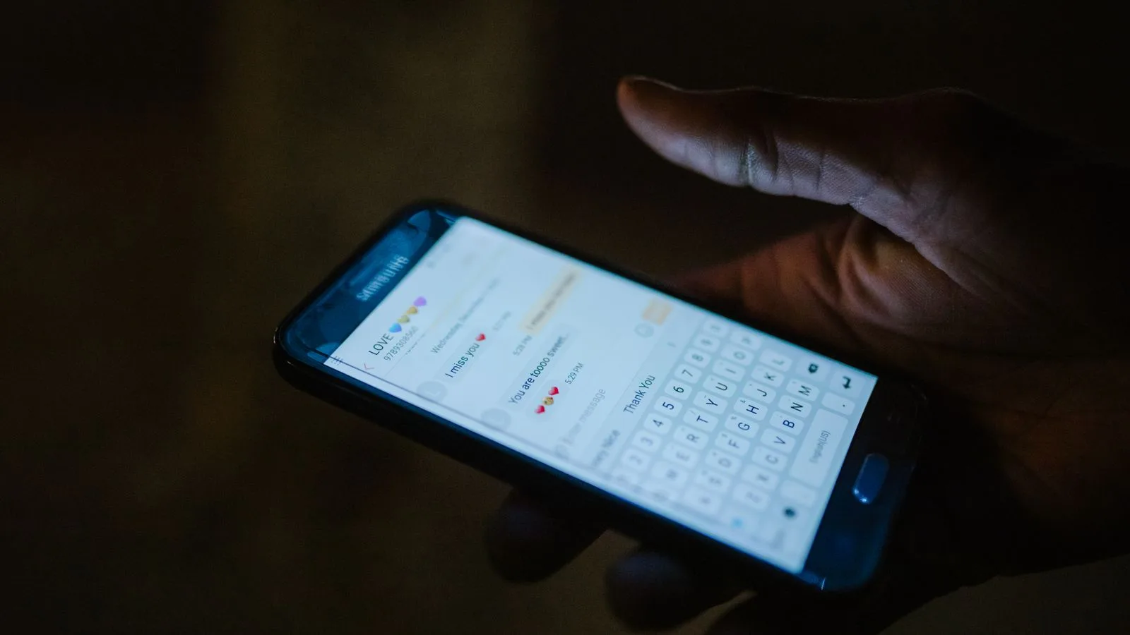 Una mano sostiene un teléfono con un chat abierto, iluminado por la pantalla en la oscuridad