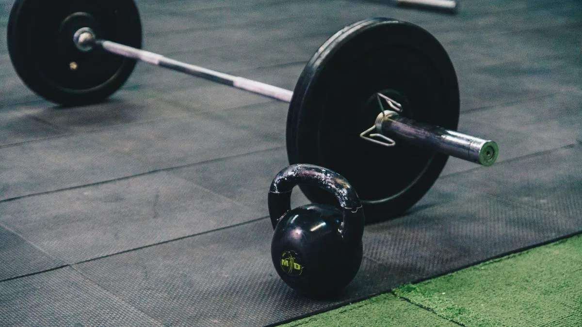 Una barra y una pesa rusa en el suelo de un gimnasio vacío