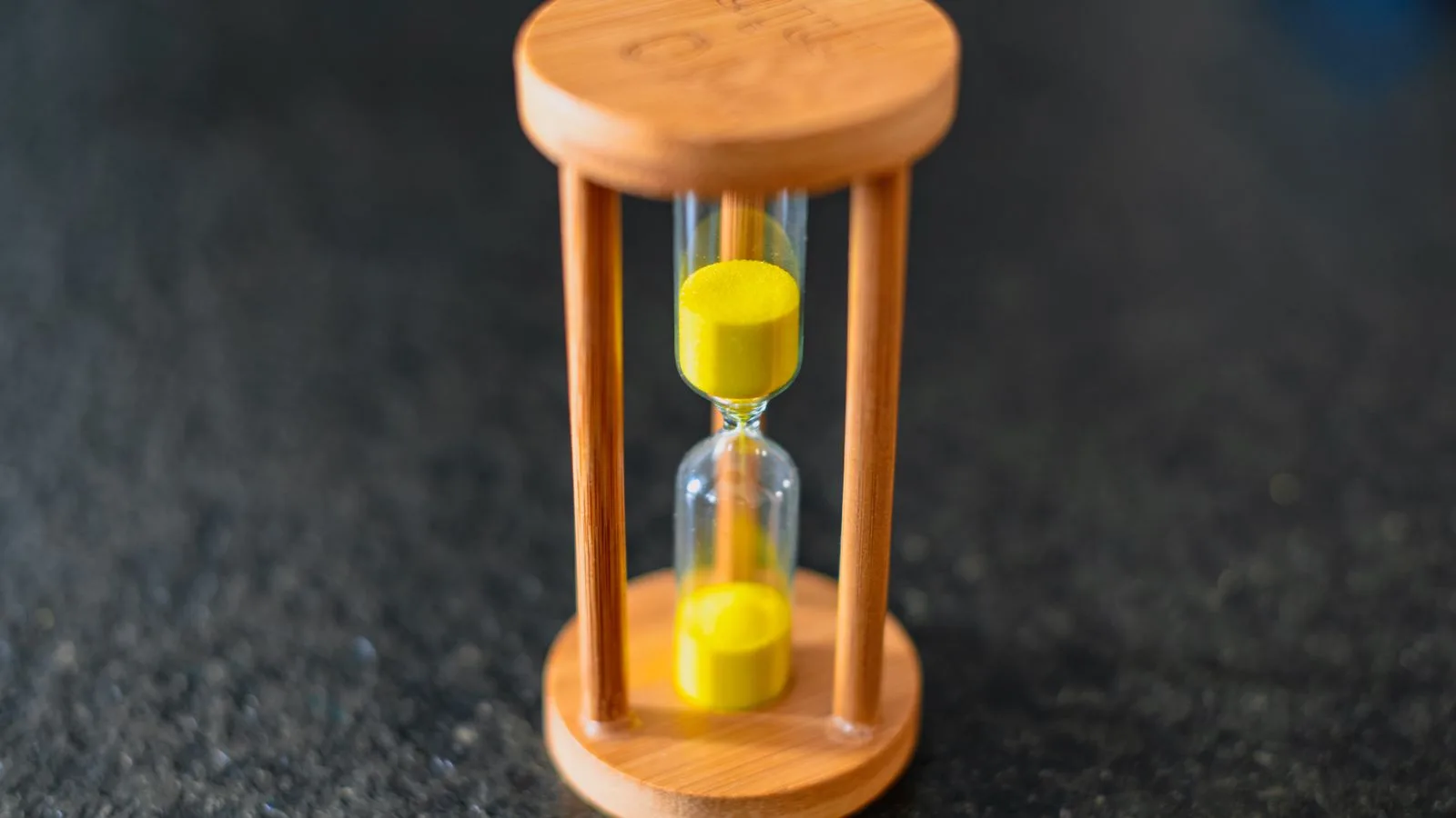 Un reloj de arena de madera con arena amarilla, sobre una superficie oscura