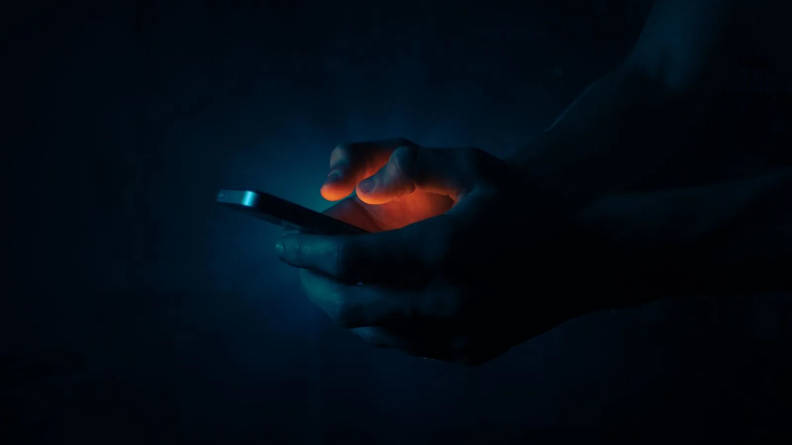 Unas manos sostienen un celular encendido en la oscuridad
