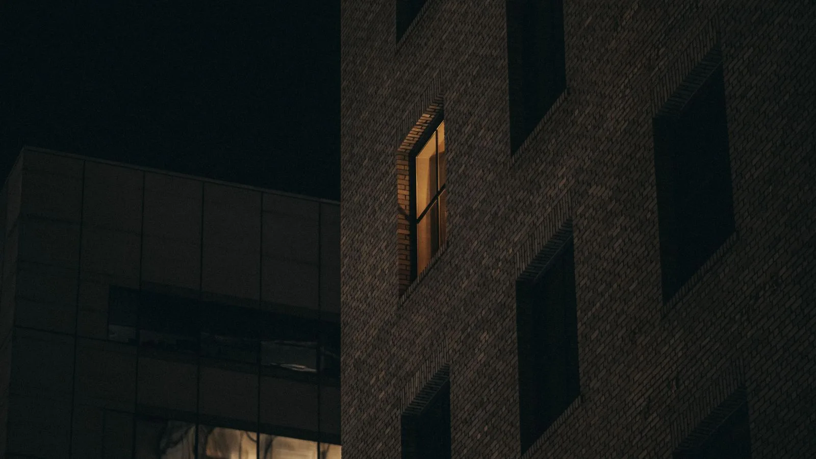Un edificio a oscuras de noche con una sola ventana iluminada