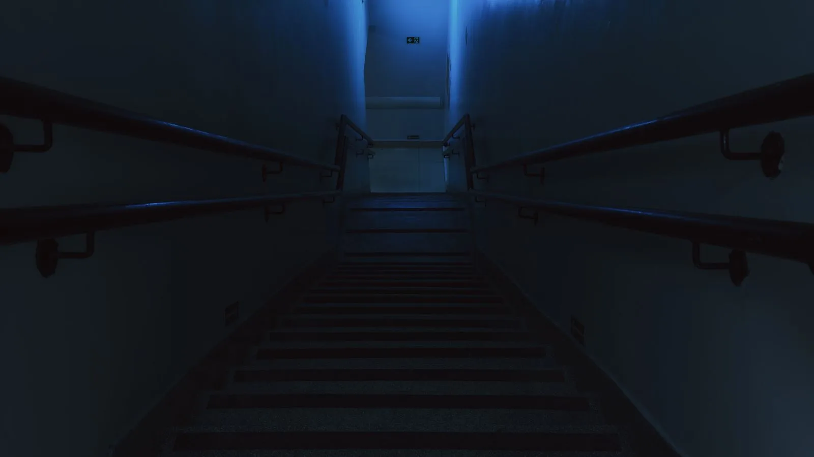 Una escalera a oscuras con una ventana iluminada al final, en la parte alta