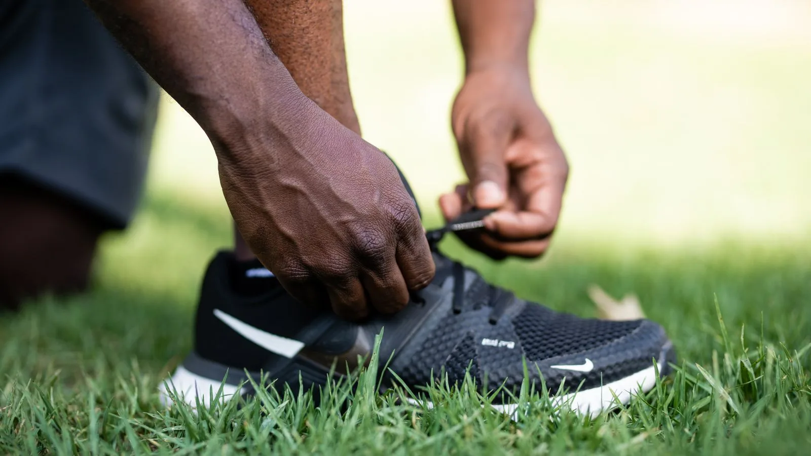 Una persona ata las agujetas de su tenis sobre el pasto, lista para empezar