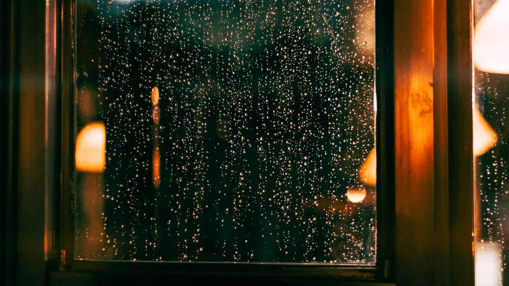 Una ventana empapada de lluvia por la noche, con las luces de la ciudad desenfocadas detrás