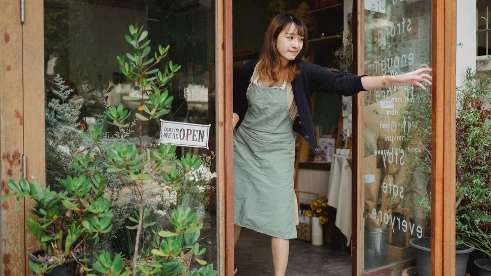 Una florista abre la puerta de su tienda, con el letrero de abierto