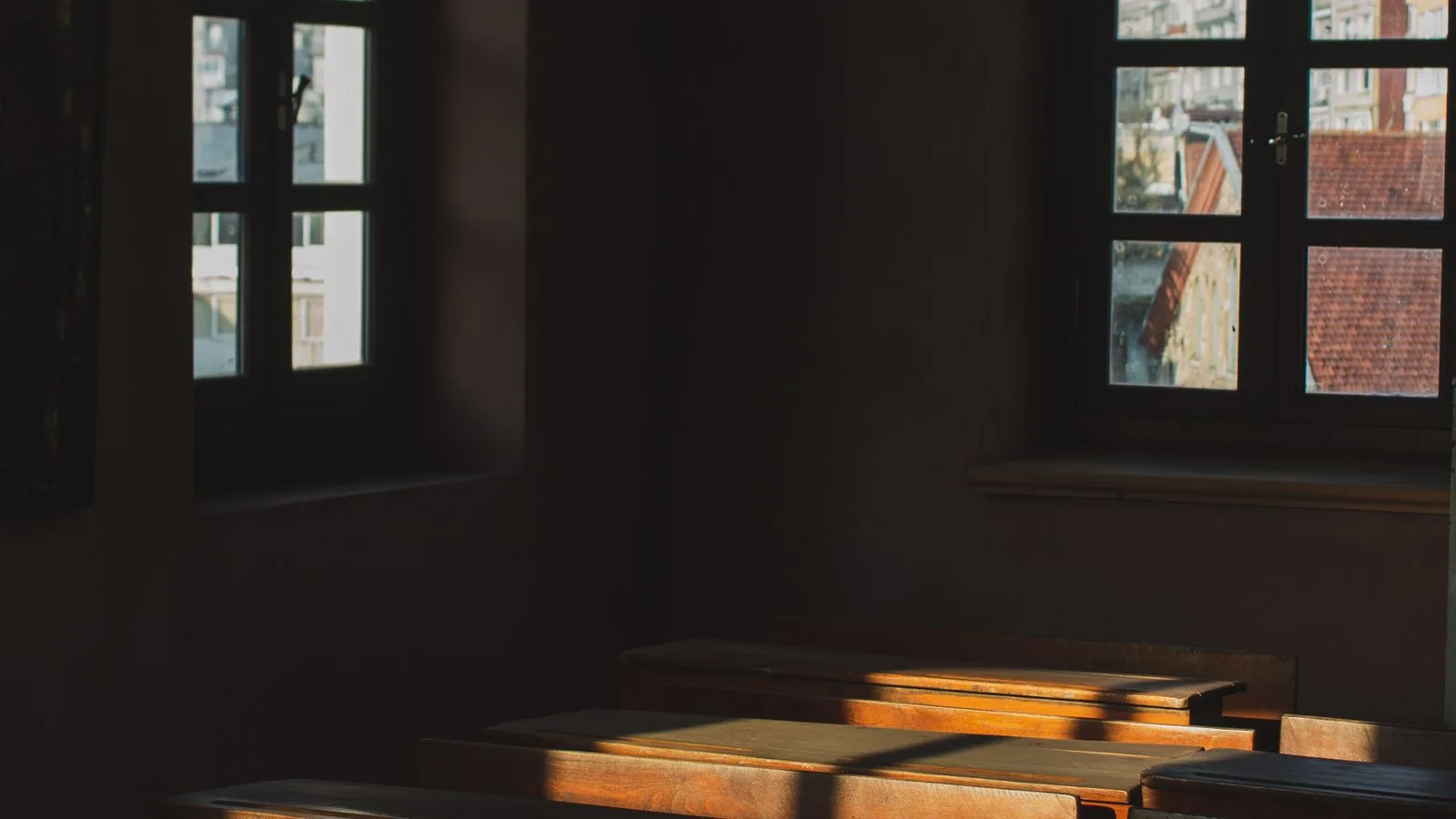 Pupitres de madera vacíos en un aula en penumbra, con la luz de la tarde entrando por la ventana