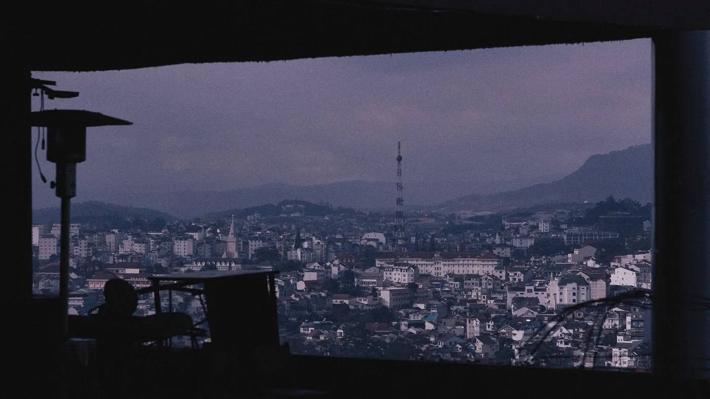 Una ciudad al amanecer vista desde una ventana en penumbra