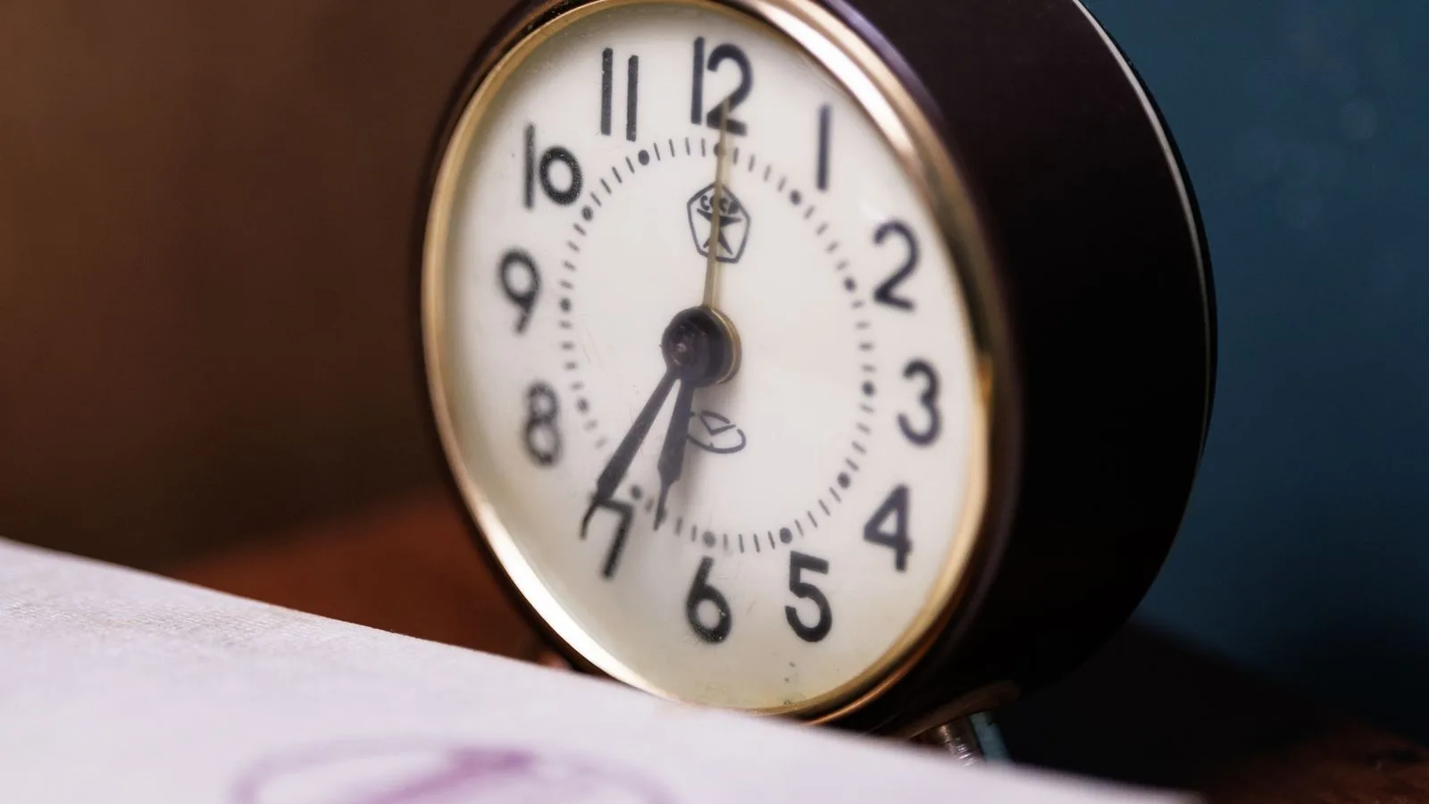 Un reloj despertador sobre un escritorio con papeles, bajo una luz cálida