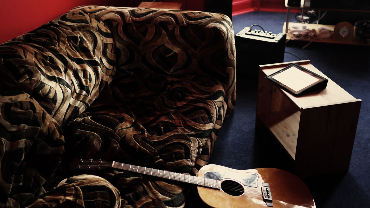 Una guitarra apoyada en un sofa, en una habitacion con luz calida