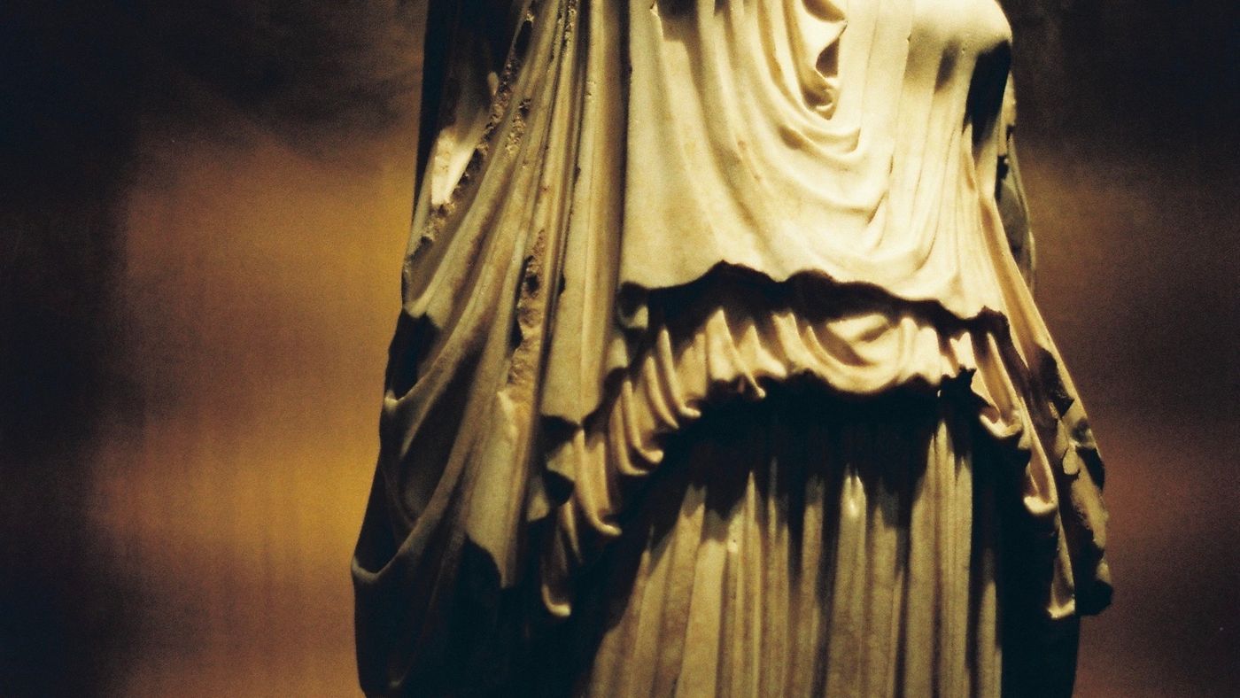 Una estatua de marmol sin cabeza iluminada en una sala oscura
