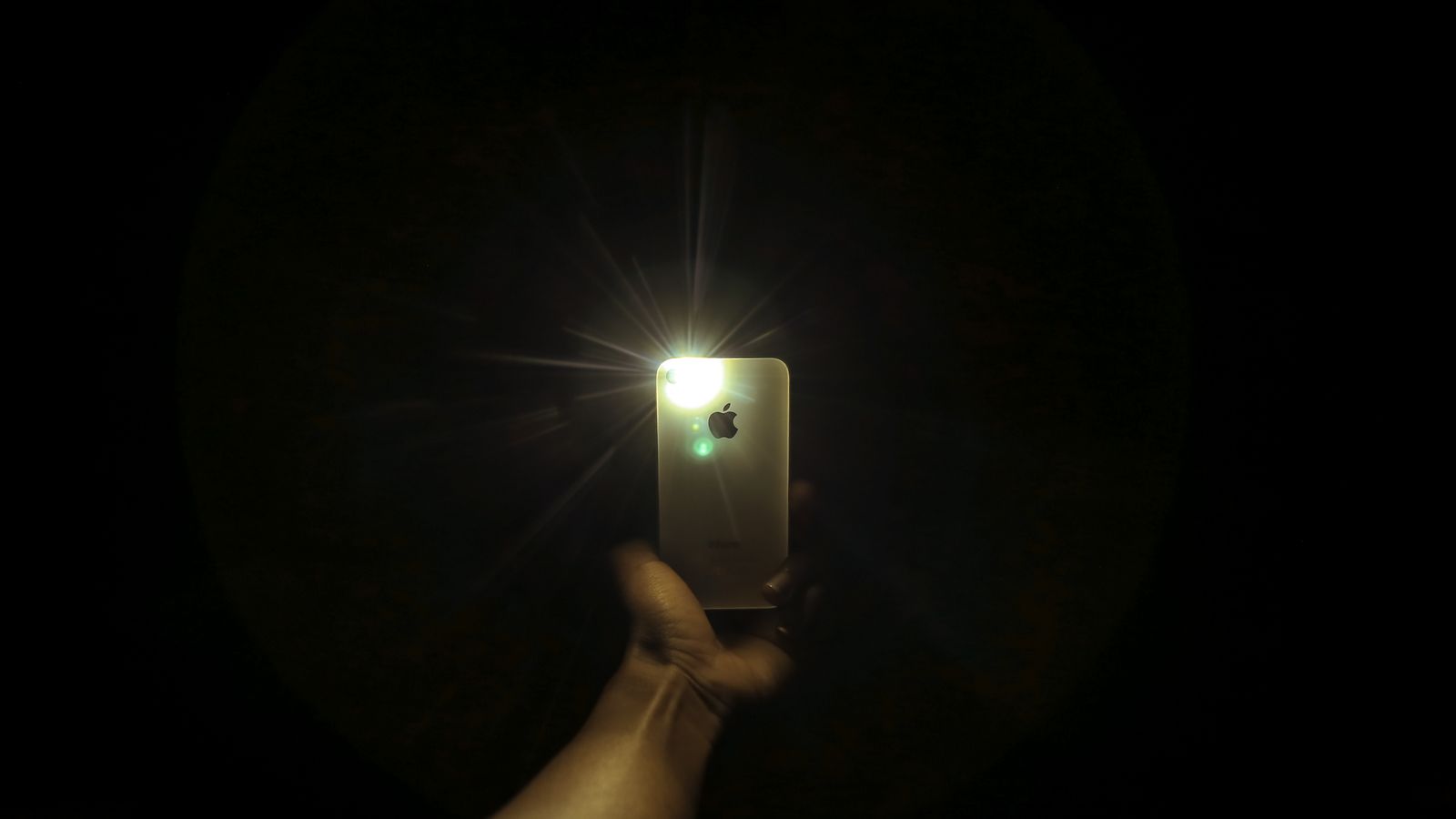 Una mano sosteniendo un telefono encendido en la oscuridad