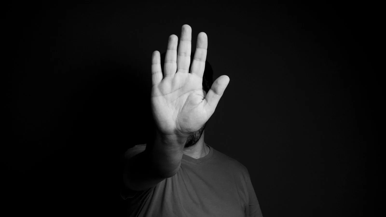 Una mano abierta en gesto de detener, sobre fondo oscuro