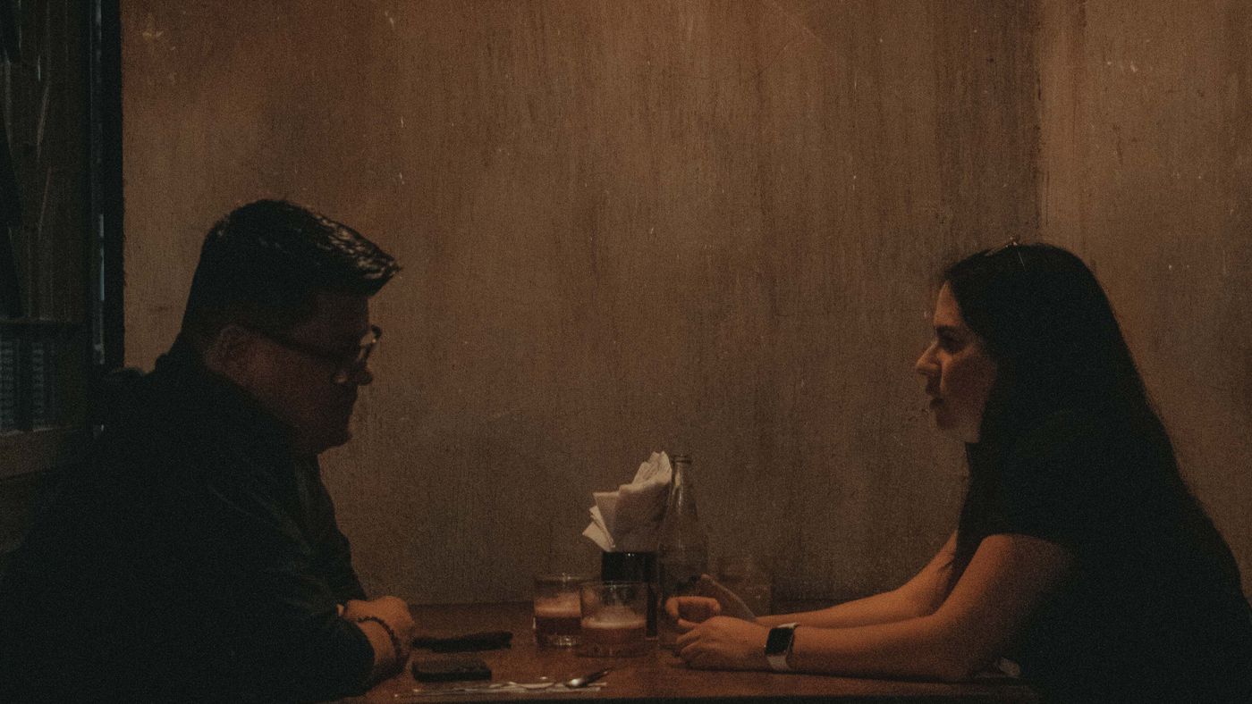Dos personas conversando en una mesa con muy poca luz