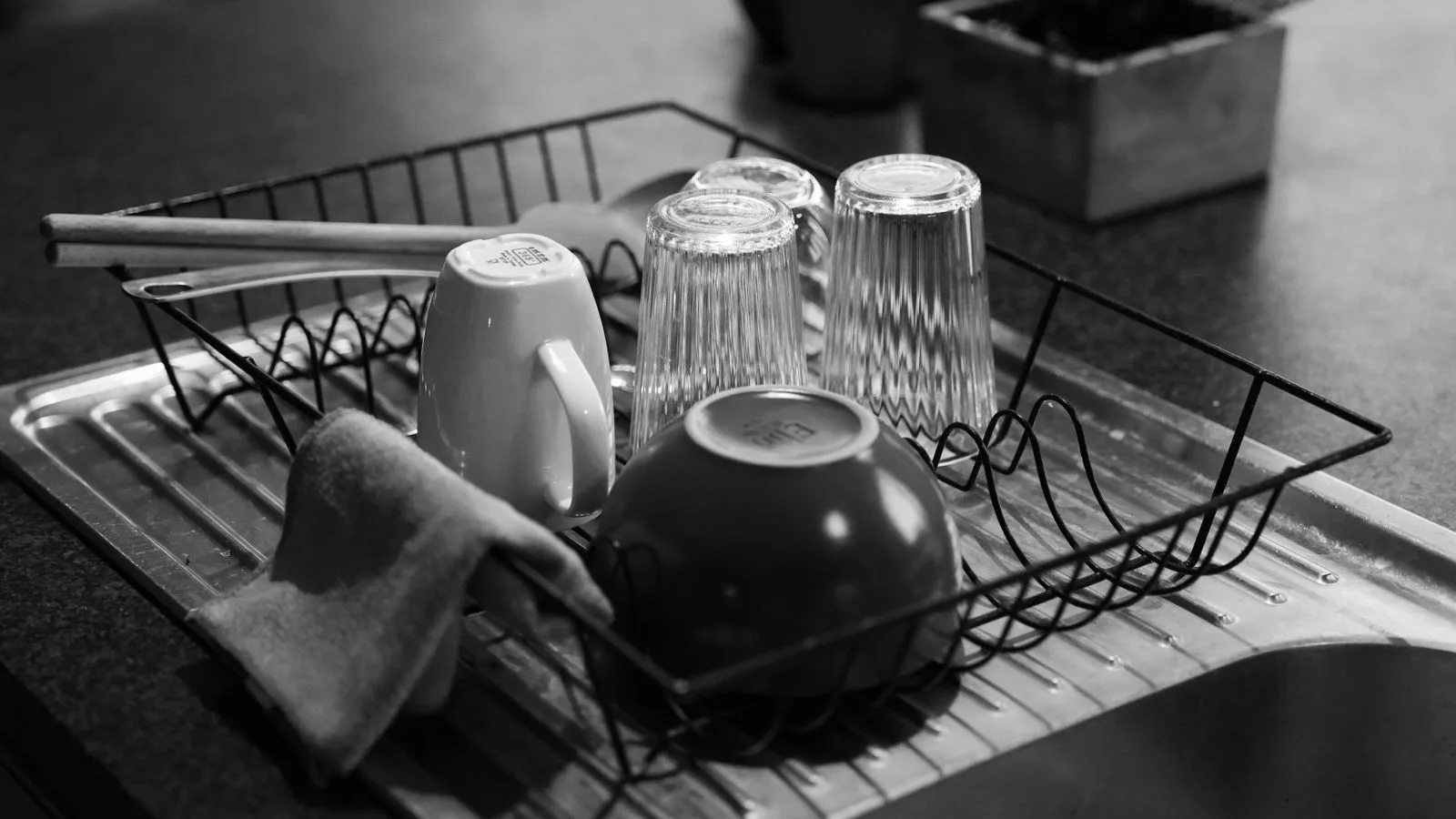 Un escurridor con tazas y vasos recién fregados sobre una encimera oscura