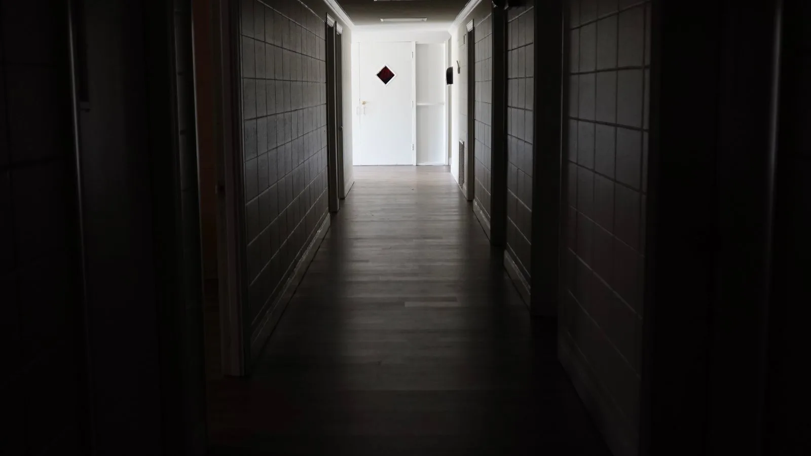 Un pasillo de casa en penumbra, con las puertas cerradas y una luz encendida al fondo