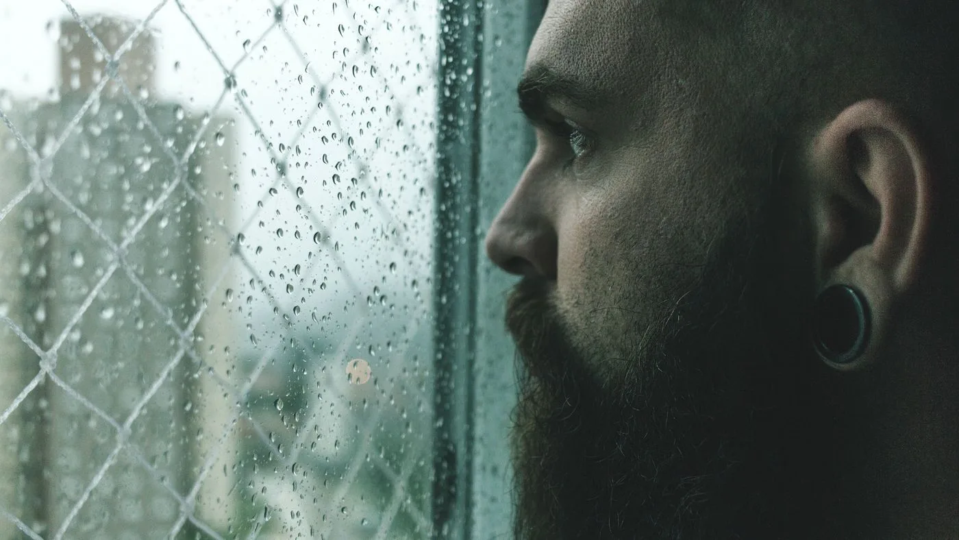 El rostro de una persona tras un cristal cubierto de lluvia