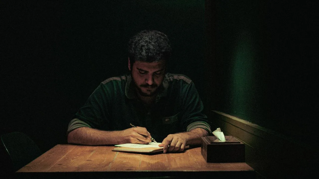 Persona escribiendo a mano en un cuaderno sobre una mesa, de noche, con una sola lámpara