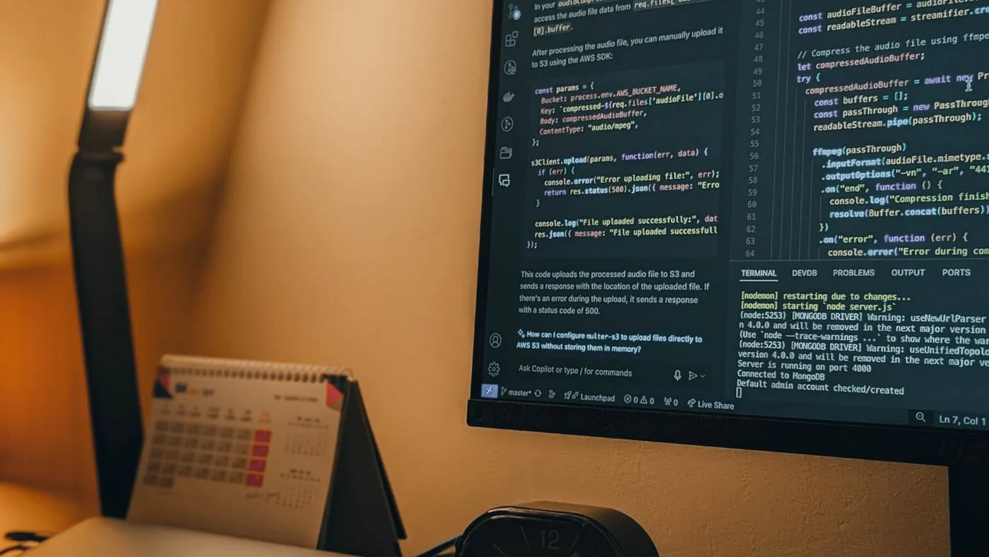 Escritorio de noche con pantalla encendida, cuaderno y una lámpara cálida